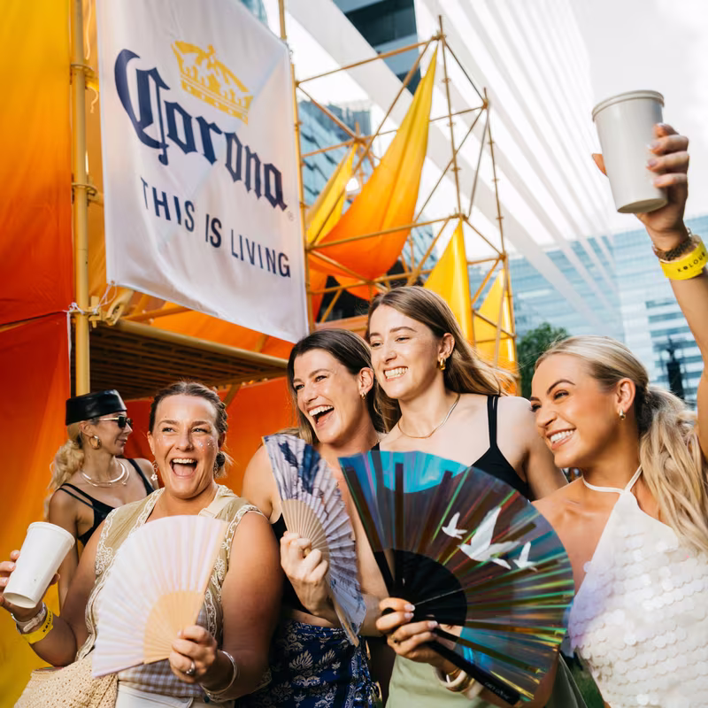 A crew of friends with fans laughing under the Corona banner at Kolour Cloud 11